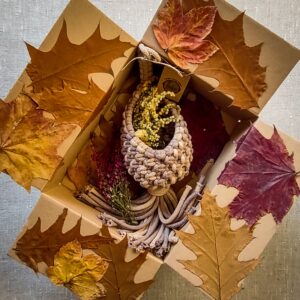Makramowy koszyczek zapakowany w pudełko wypełnione jesiennymi, kolorowymi liściami.