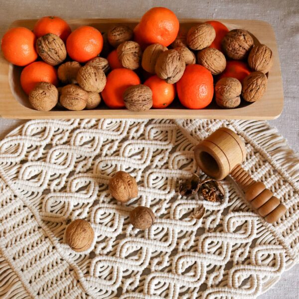 Na makramowej serwecie drewniany talerz z mandarynkami i orzechami