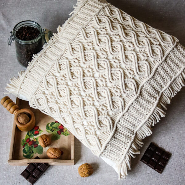 Makramowa poduszka w otoczeniu ziaren kawy, tacy z orzechami, czekolady