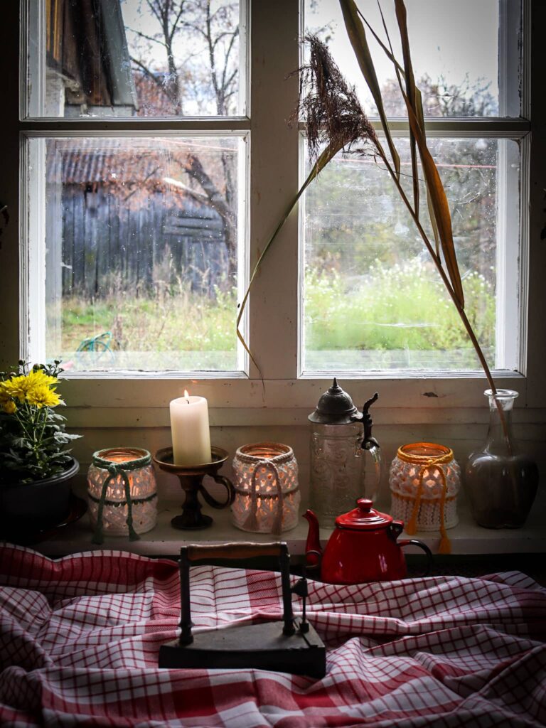 Na tle okna starej chaty lampiony, stare szklane wazoniki, dzbanek i żelazko na serwecie