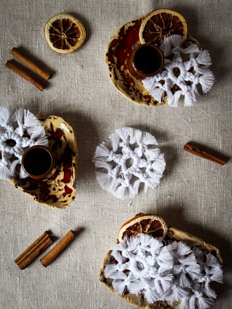 Śnieżynki rozłożone na ceramicznych naczyniach, jak ciasteczka na deser. Scena ozdobiona pomarańczkami i cynamonem