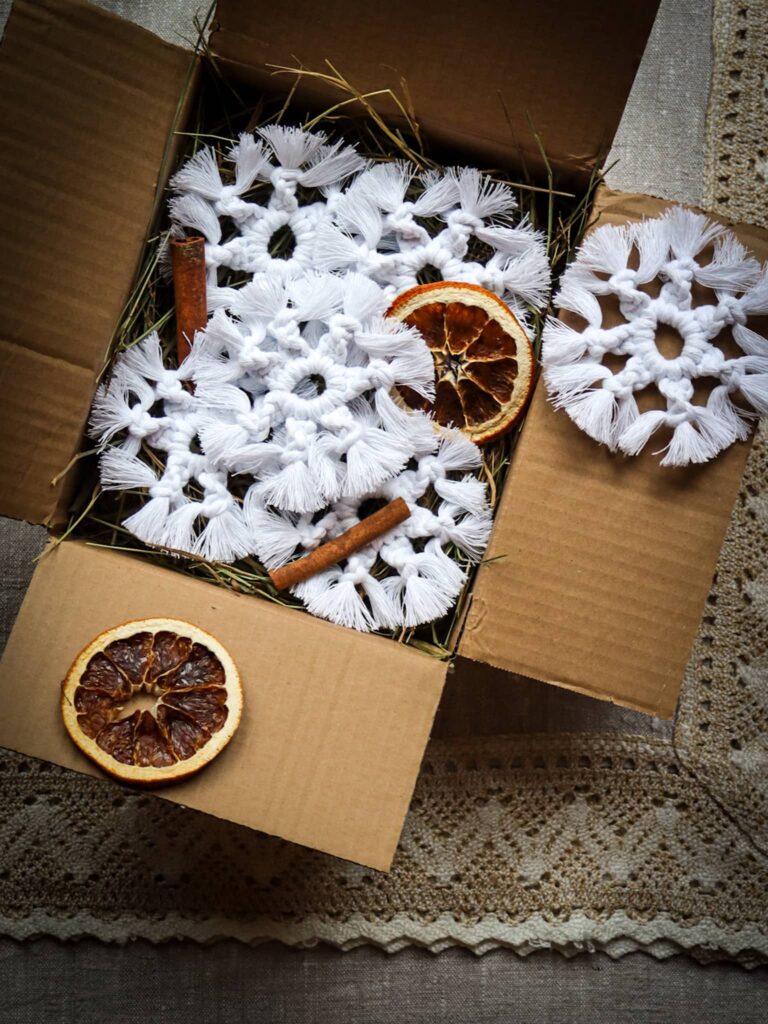 Box świąteczny ze śnieżynkami - leżą w pudełku na sianku ozdobione pomarańczkami i laskami cynamonu