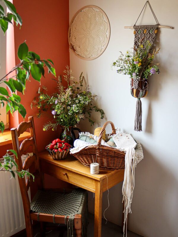 Na stoliczku wazon z polnymi kwiatami i truskawki, oraz kosz ze sznurkami, nad - bukiet w kwietniku etno oraz mandala, obok krzesło