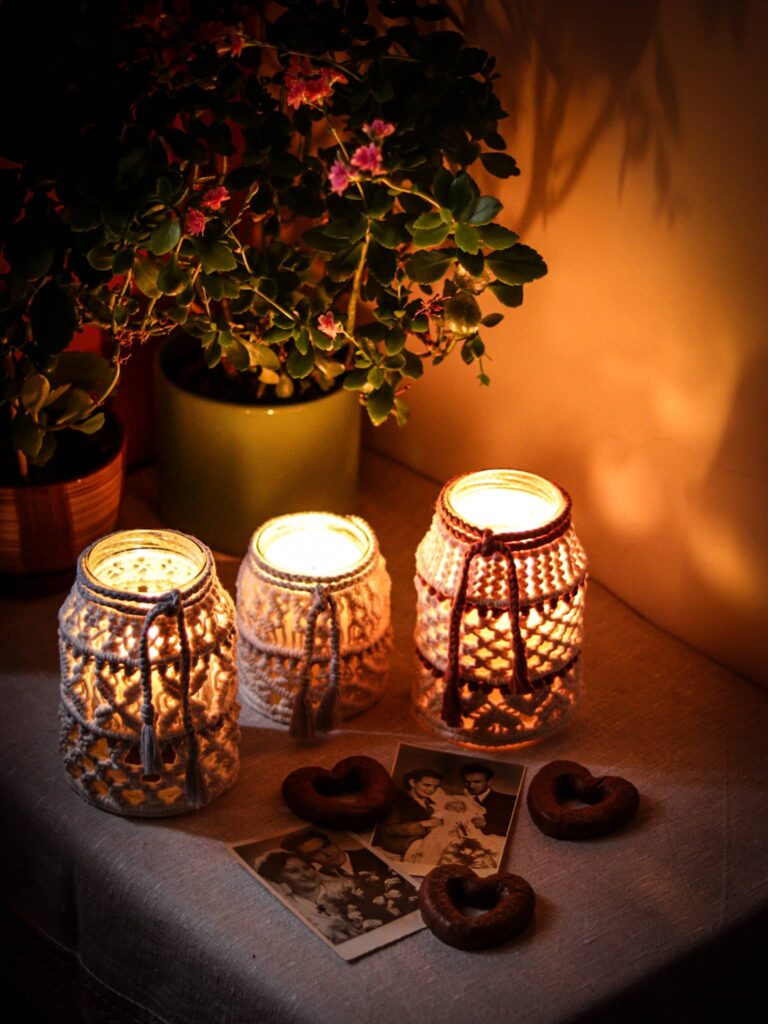 Trzy lampiony świecą po zmroku na stoliku, z cienia wyłania się kwiat i stare fotografie