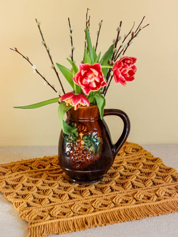 serweta musztardowa w jodełkę, a na niej dzbanek z tulipanami